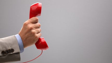 Photo of a hand holding up a red telephone handset.